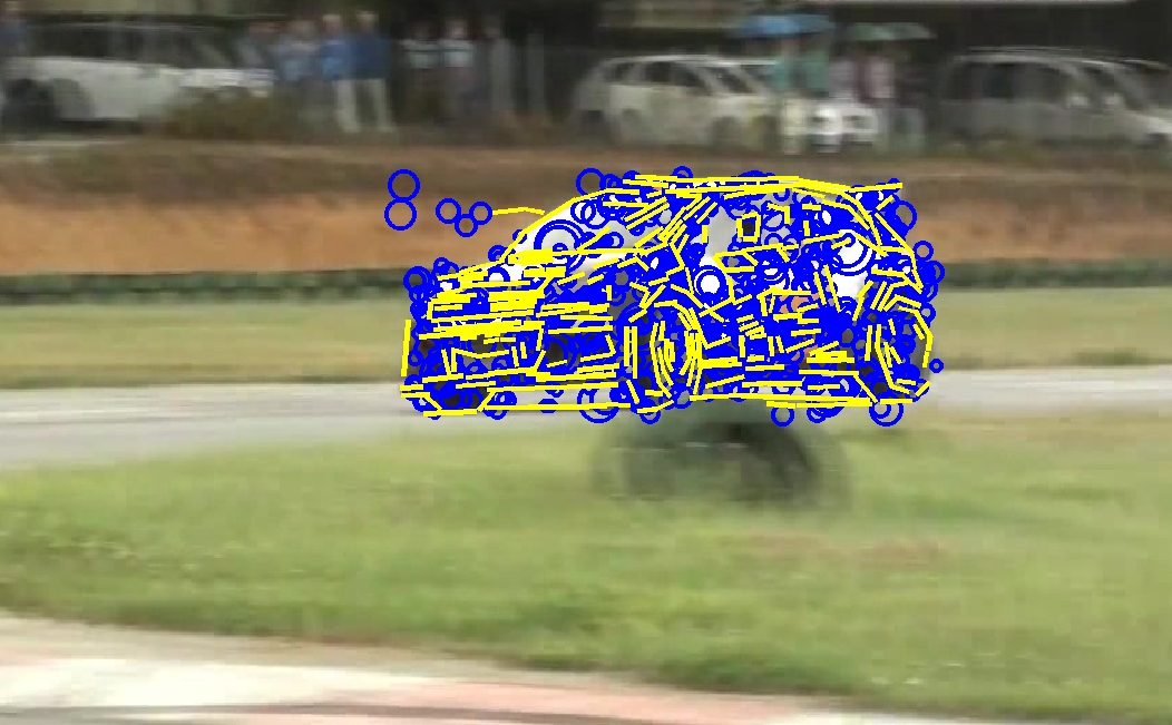 Photo of a car (an early frame from the Rally-VW sequence) with overlaid blue circles standing for 2D point features and yellow line segments for 2d line features.